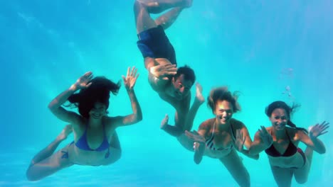 amigos saludando a la cámara bajo el agua en la piscina juntos