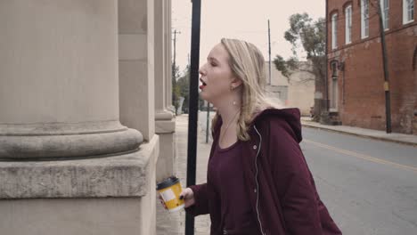 slow motion of a young female crossing the street while singing to herself and holding a hot beverage in her hand