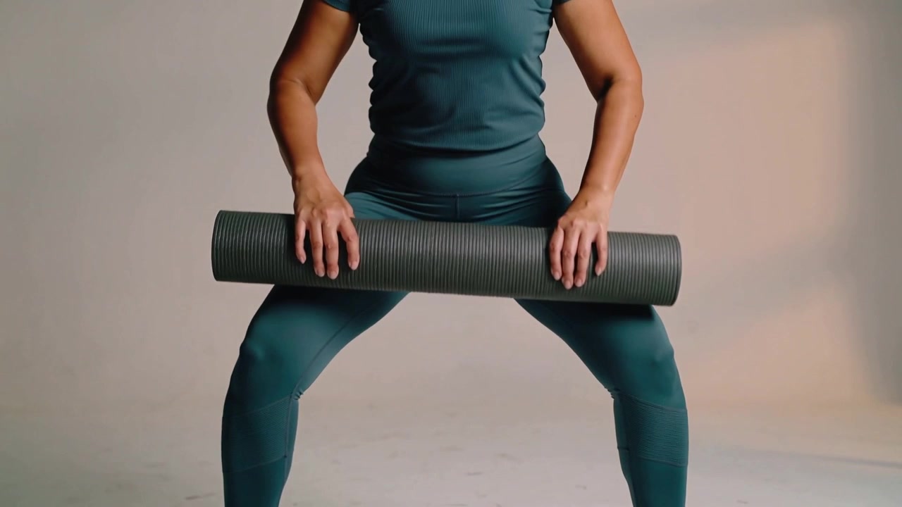 Starting wide-stance teal-clad woman lowering hips into squat at studio, holding mat for workout