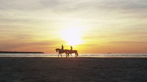 silhouette of two riders on horses at beach in sunset light.