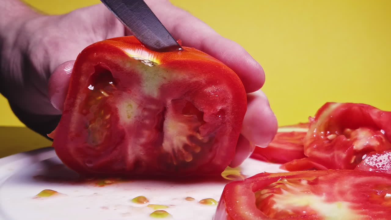 Close-up shot of a man cutting tomato on the desk in slowmotion in front of a yellow background