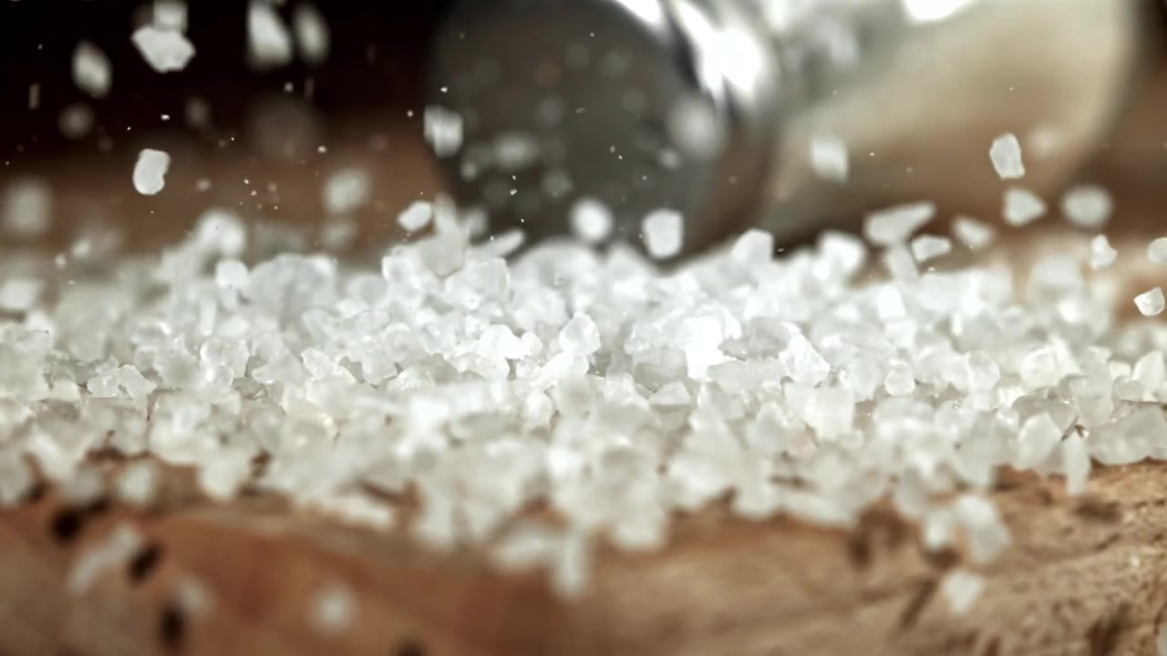 Grove havsaltkrystaller falder ned på en træoverflade i slowmotion