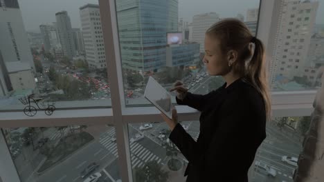 Mujer-De-Negocios-Usando-El-Panel-Táctil-Junto-A-La-Ventana-Con-El-Paisaje-Urbano-De-Seúl,-Corea-Del-Sur