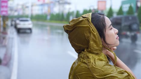 asian girl wear yellow raincoat on the raining day standing on the road side, rainy season weather climate pouring rain, bad luck get wet while going out for work, car and motorcycle passing by