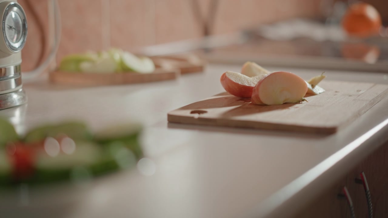 Halved onion and sliced pieces rest on wooden cutting board while visible hand movement above surface suggests active chopping during meal prep in warm soft kitchen light, creating rustic home
