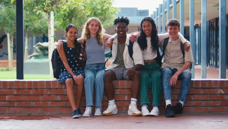 Portrait-Of-Smiling-Multi-Cultural-High-School-Or-Secondary-Students-Sitting-On-Wall-Outdoors