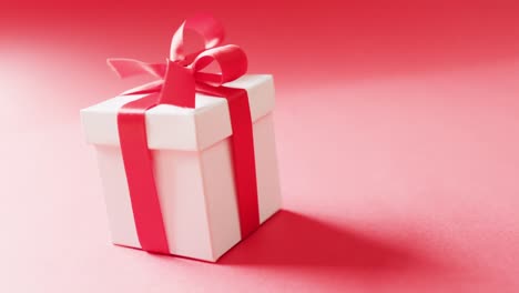 Video-of-white-gift-box-ties-with-red-ribbon,-on-red-background,-with-copy-space