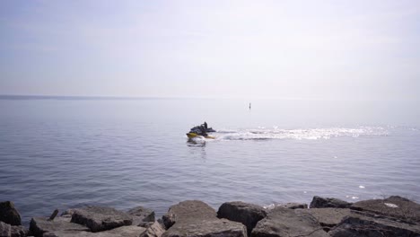 jet skis in lake ontario, canada. jet ski on water personal watercraft fast boat sea doo driving in water in toronto, ontario, canada near rocky stone shore beach
