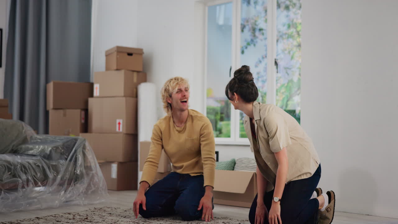Young Couple Unrolling Rug and High-Fiving in Their New Home