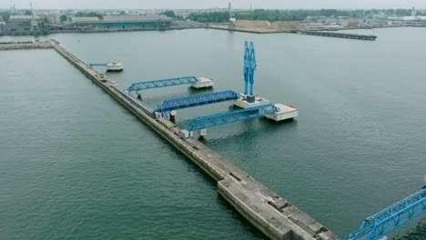 aerial establishing view of port cranes and empty loading docks at port of liepaja , liepaja city in the background, overcast summer day, wide drone shot moving backward, tilt up