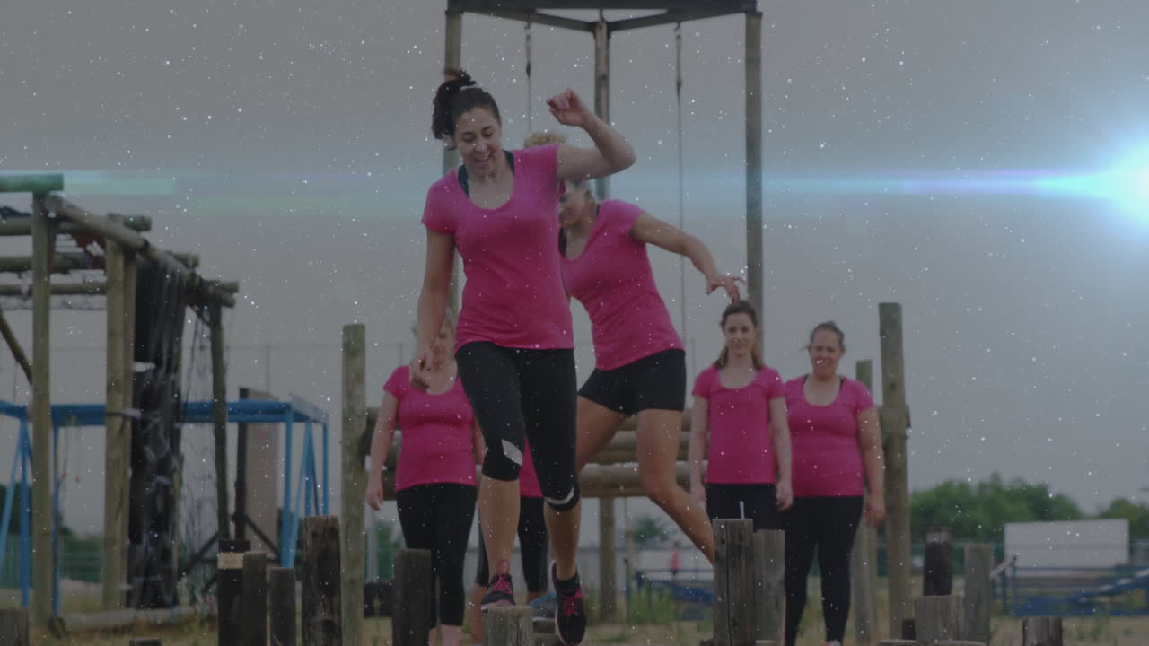 Balancing on outdoor obstacle course, women in pink shirts showing determination