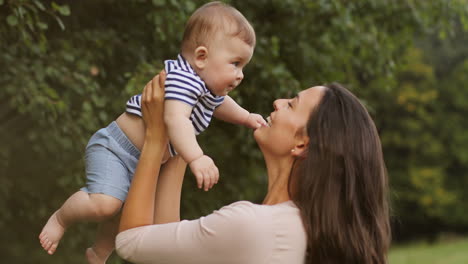 retrato de una hermosa joven madre sosteniendo y levantando a su hijo feliz en el parque