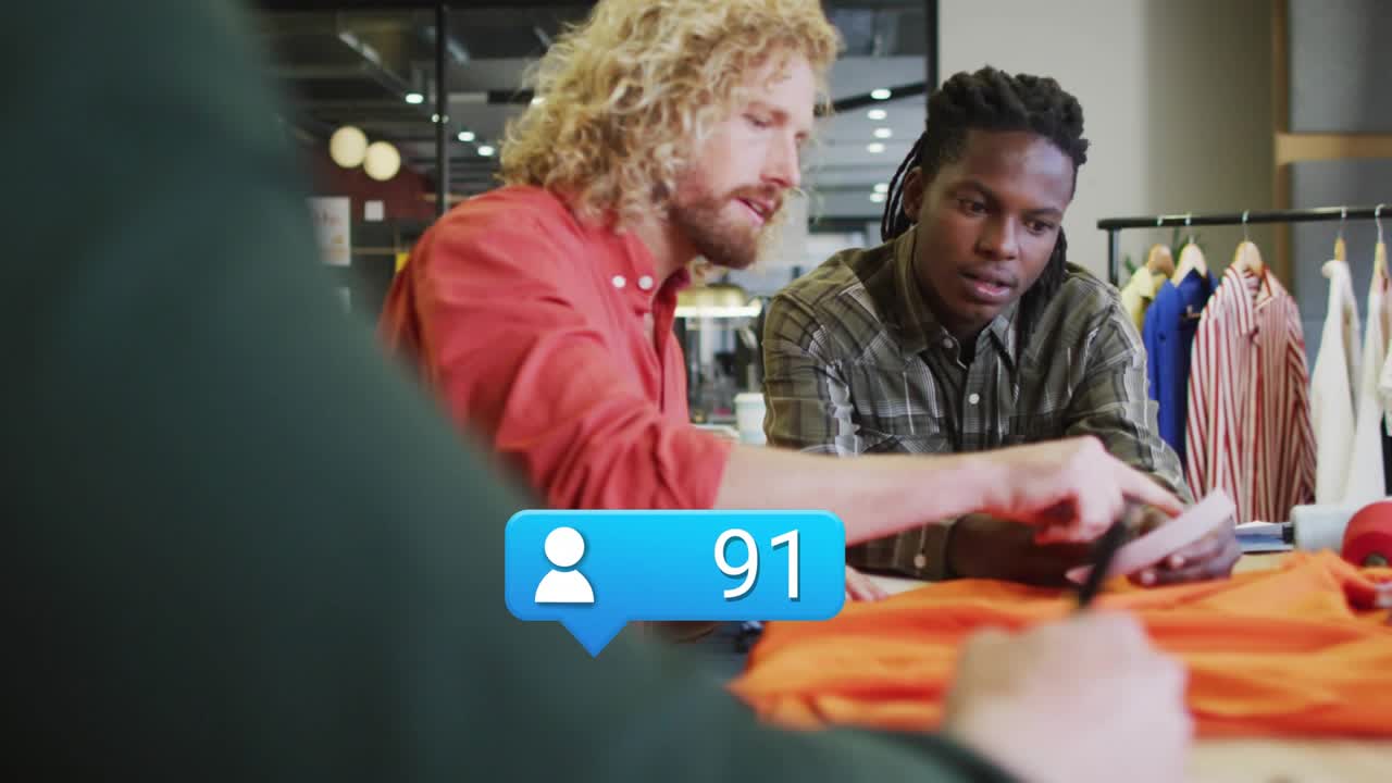 Fashion designers scrolling tablet and examining orange garment, UI bubbles updating count