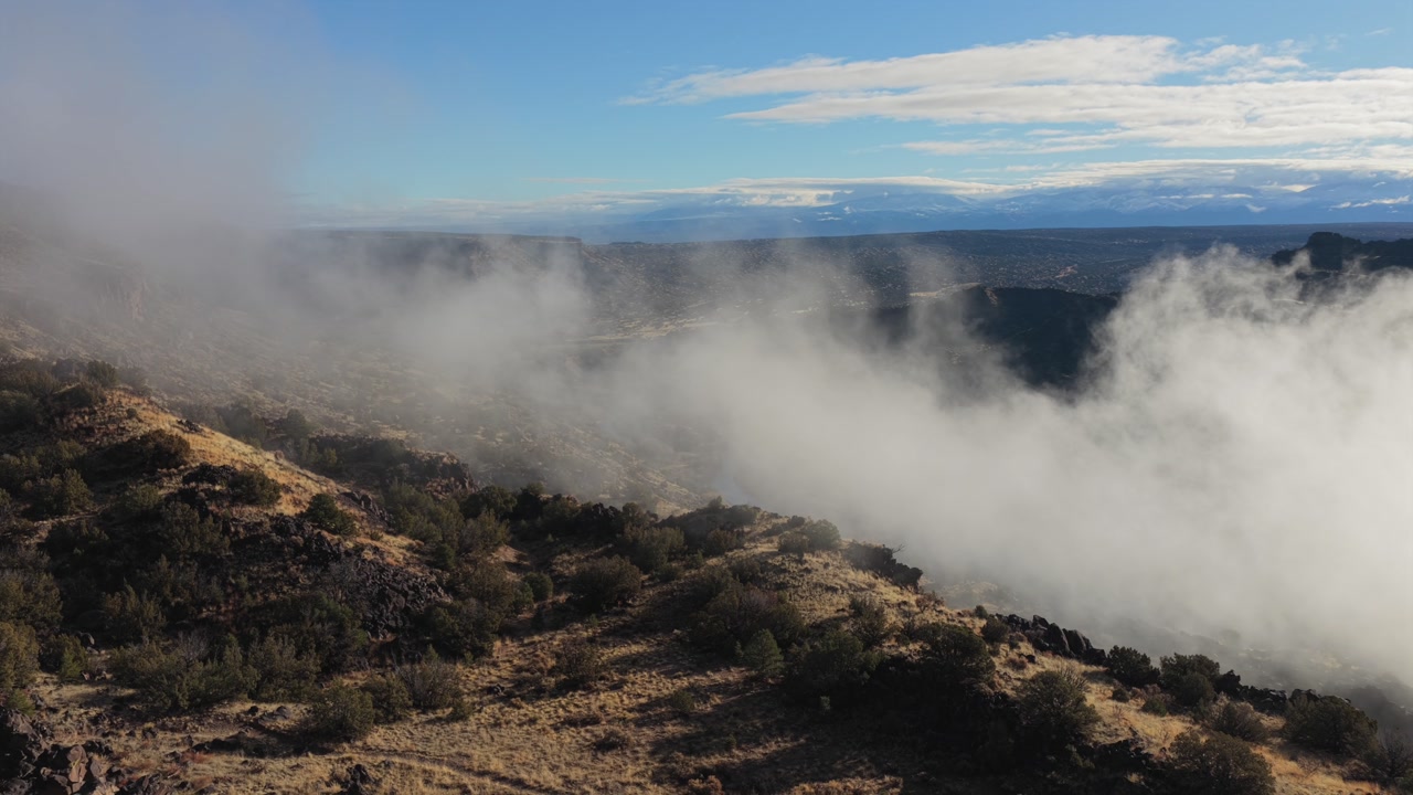 Dramatic white mist is shown forming and drifting through a deep rocky canyon landscape. The footage captures the atmospheric weather patterns as clouds develop within the rugged wilderness gorge.