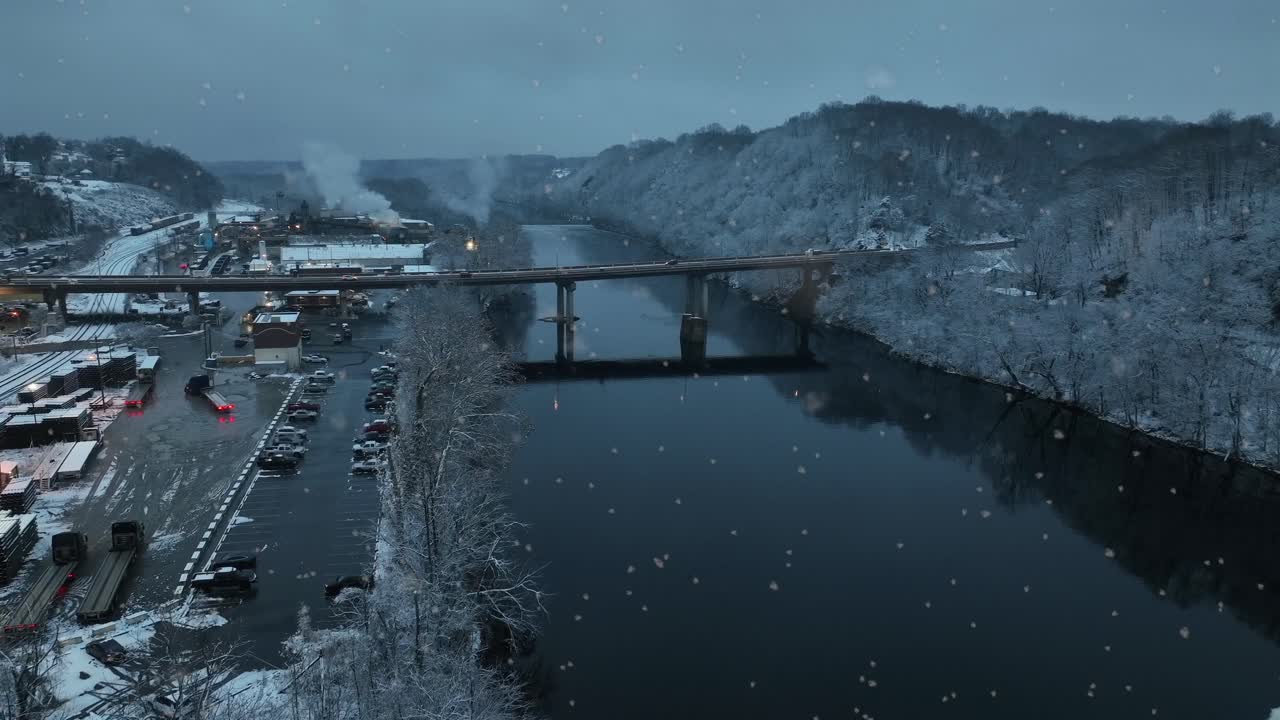 Vista aerea invernale di Lynchburg, Virginia, che mostra un fiume coperto di neve con fontana, ponte, linee ferroviarie e colline circostanti durante una nevicata calma e suggestiva. Inquadratura ampia
