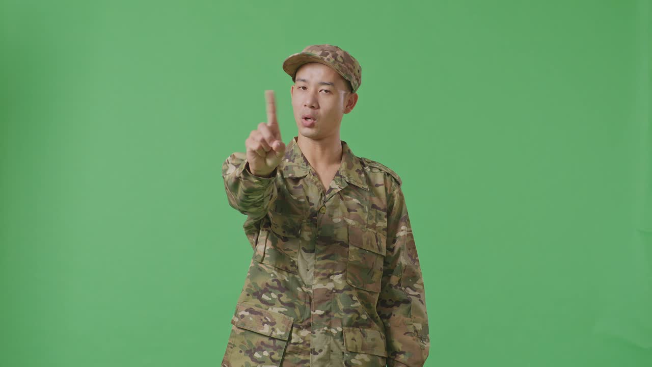 Asian Man Soldier Pointing At You And Disapproving With No Index Finger Sign While Standing In The Green Screen Background Studio