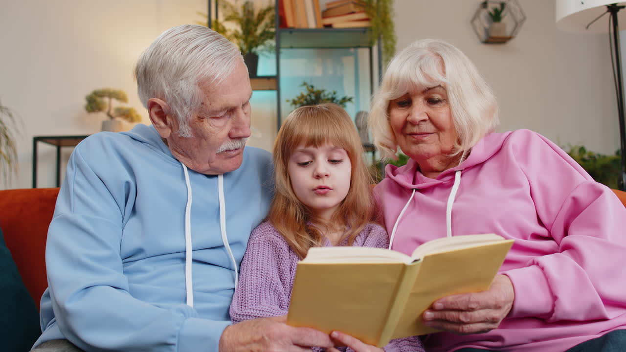 Nonni caucasici e nipote leggono insieme un libro interessante seduti sul divano
