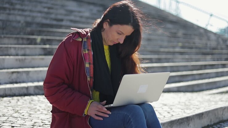 Eftertænksom kvinde sidder på fortovet med laptop på skødet