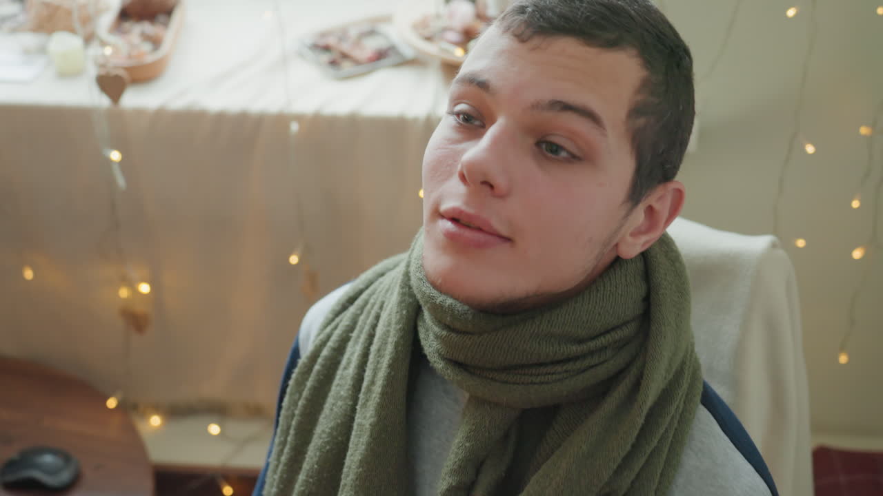 Studente caucasico che indossa sciarpa verde e occhiali da sole, luce soffusa dalla finestra, bokeh caldo, sorriso rilassato, arredamento vintage, tavolo con tazza, primo piano spontaneo, atmosfera lifestyle, prova di un accessorio elegante, sottile.