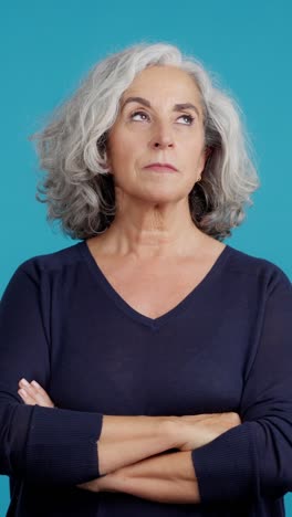 serious senior woman with gray hair and crossed arms on blue background