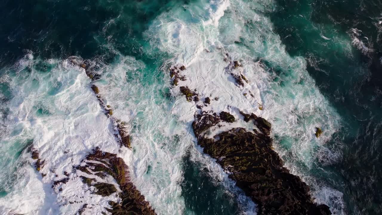 Vista aerea di rocce vulcaniche scure in contrasto con onde bianche spumeggianti e acque atlantiche di un blu intenso lungo la frastagliata costa di Ferraria nelle Azzorre.