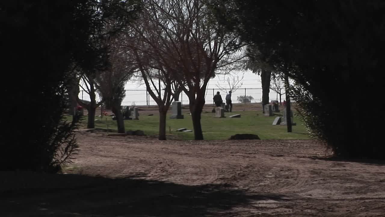 dos personas caminan y miran lápidas en un cementerio junto al mar