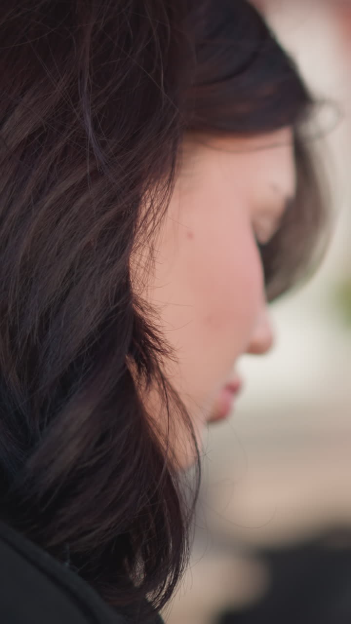 어두운 갈색 머리카락을 가진 젊은 여성의 측면 프로파일 부드러운 초점, 생각에 빠진, 배경에 흐릿한 건축 구조