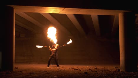dos tipos del espectáculo de fuego están girando cadenas de fuego por detrás. el tipo de delante está respirando fuego