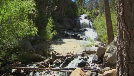 A-moving-shot-past-a-tree-to-reveal-a-beautiful-alpine-waterfall-1