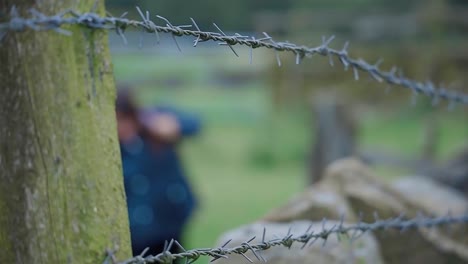 out of focus walker, hiker puting on her rucksack, shot through a farmland fence and stone wall