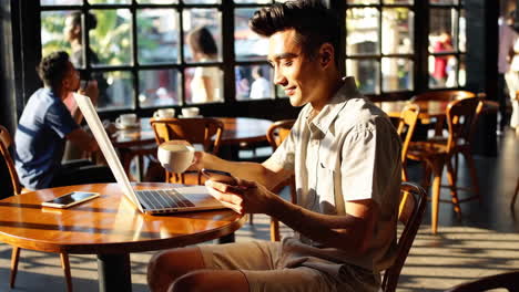 young man working or relaxing in a cafe with a laptop and phone
