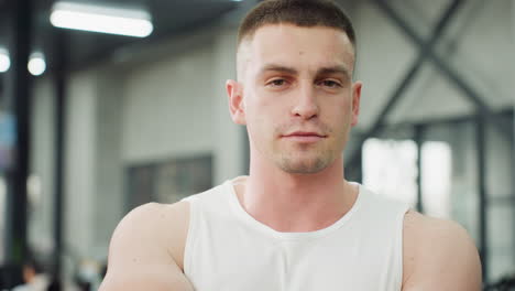 portrait view of fitness expert standing in modern gym, wearing white tank top, looking ahead with calm expression while overhead lights blur in background conveying healthy lifestyle focus