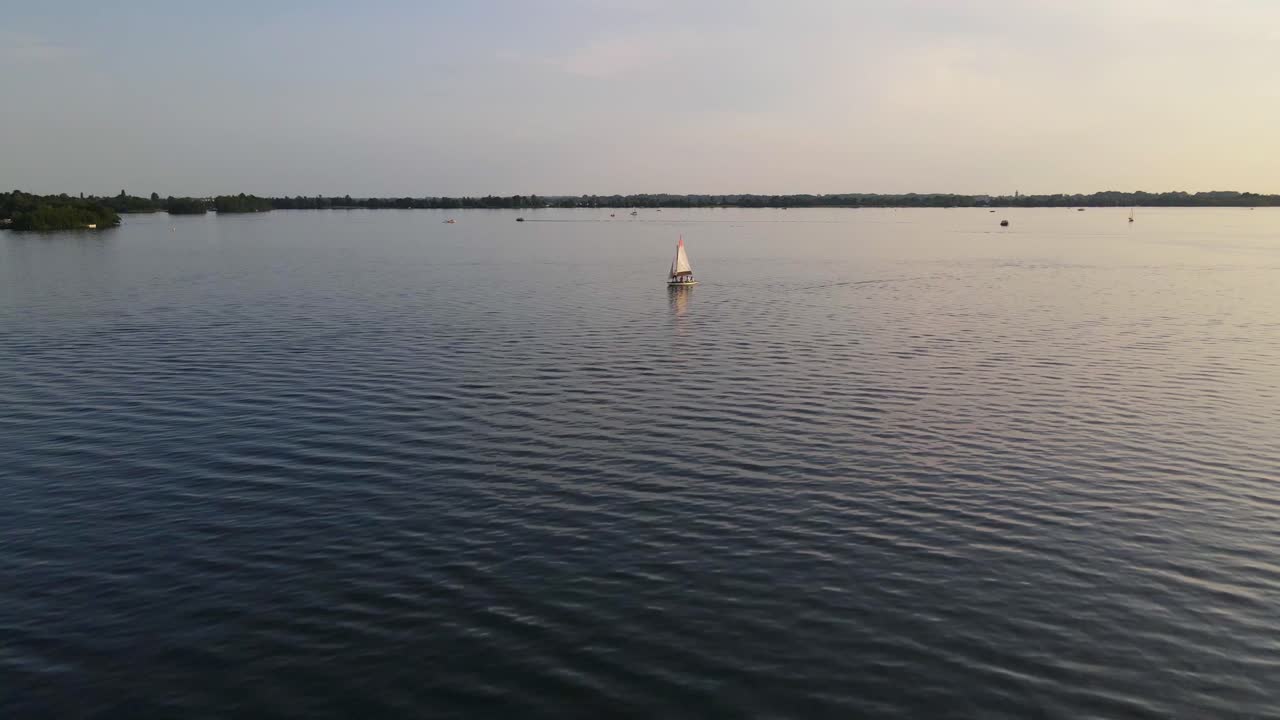 una tranquila puesta de sol sobre el lago wijde blik, países bajos, con un velero a la deriva suavemente a través de las aguas tranquilas, ofreciendo una vista serena y tranquilizadora de la naturaleza en su mejor momento.