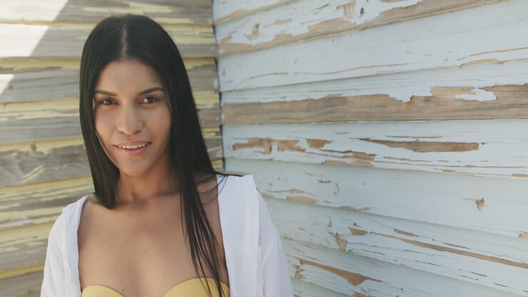 Ritratto di donna ispanica sorridente davanti a una parete di legno invecchiata sotto il sole, spazio per il testo, al rallentatore.
