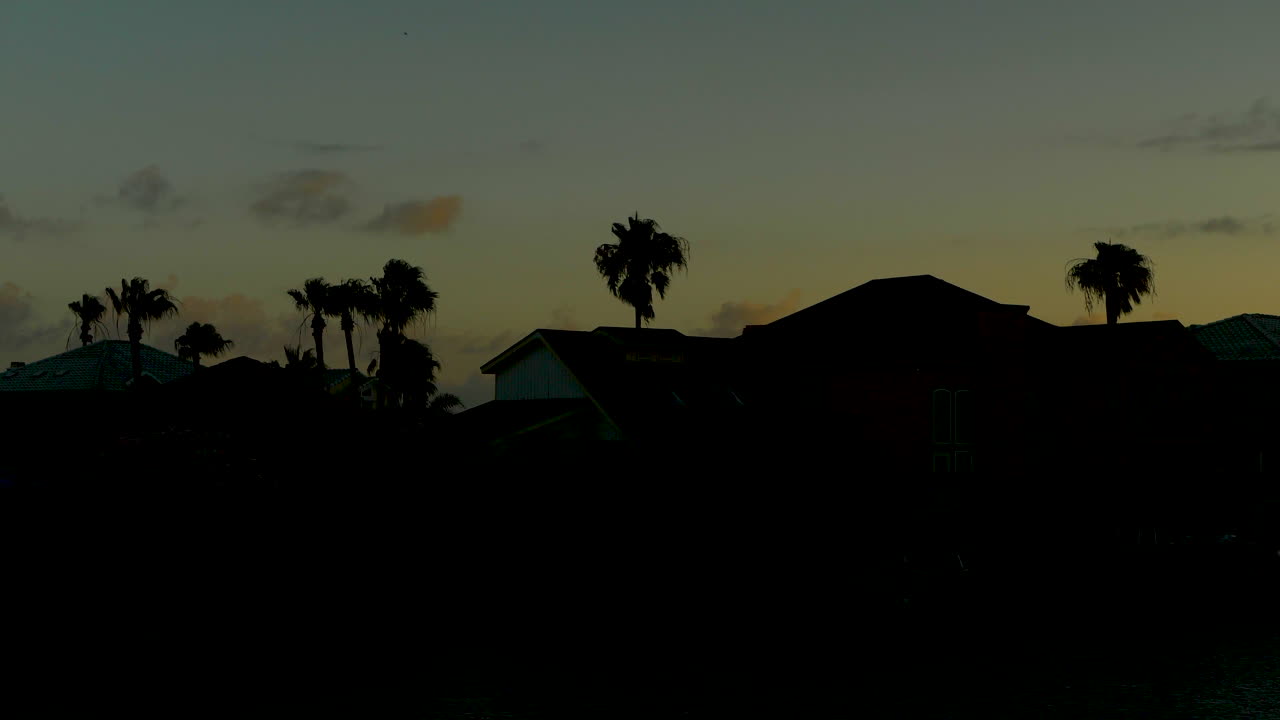 puesta de sol frente a la costa de texas detrás de casas y árboles silueteados