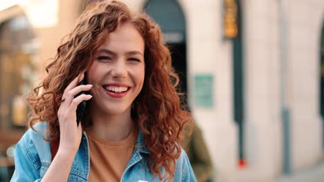 vista cercana de una mujer pelirroja sosteniendo café para llevar y hablando por teléfono inteligente en la calle