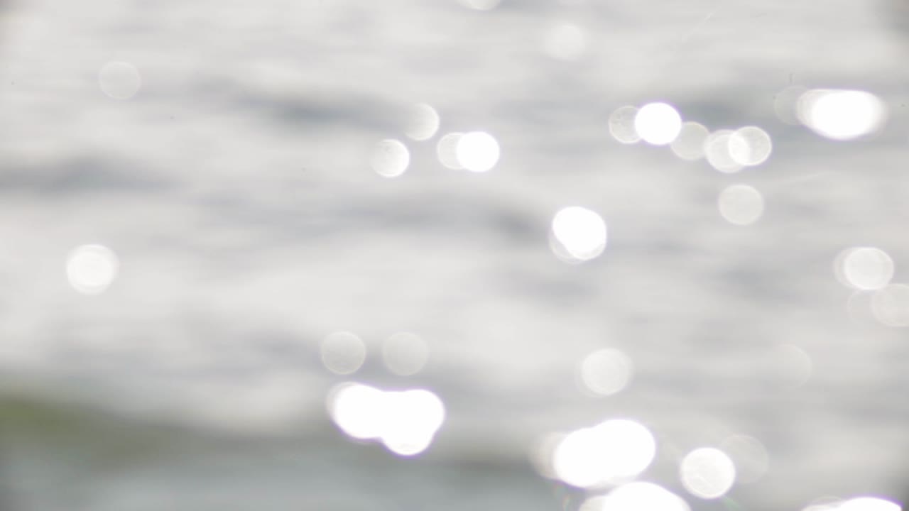 Beautiful Scenery Of A Calm Sea Waves With Bokeh Lights During Sunny Day - Close Up Shot