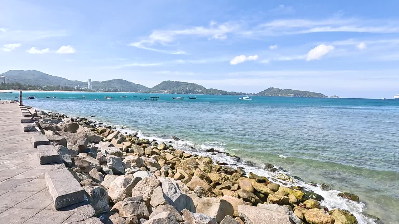 A tranquil seaside path with clear blue waters and rocky shoreline under bright daylight at Kalim Beach, Phuket