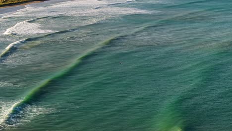 un surfista solitario se sienta esperando en el medio de la bahía mientras las olas cruzan y se rompen