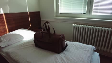 a brown travel bag was laid in a hotel room lit by the morning sun