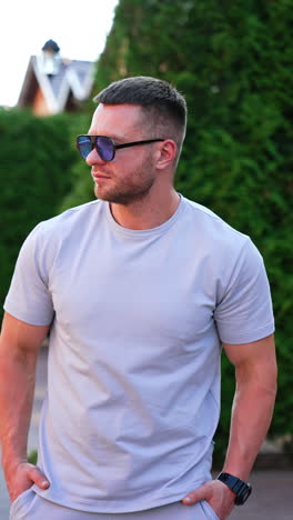 muscular caucasian man wearing sports clothes and sunglasses stands outdoors. portrait of a handsome sportive male on the paved road. vertical video