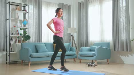 una chica de fitness asiática en ropa deportiva está haciendo ejercicios de lanzamiento hacia adelante en su sala de estar con un interior moderno
