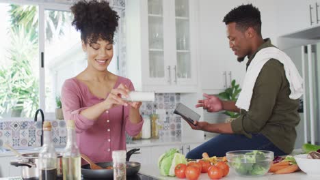 una feliz pareja afroamericana cocinando y usando una tableta en la cocina.