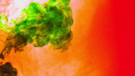 Green-And-Orange-Paint-Or-Dye-Dropped-Into-Water-Against-White-Background-To-Create-Swirling-Colourful-Smoke-Background