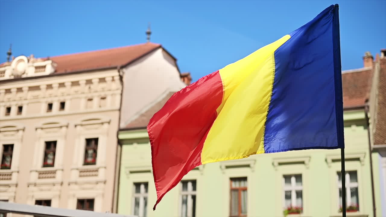 La bandiera nazionale che sventola al vento con vecchi edifici residenziali sullo sfondo a Brasov, Romania. Movimento lento