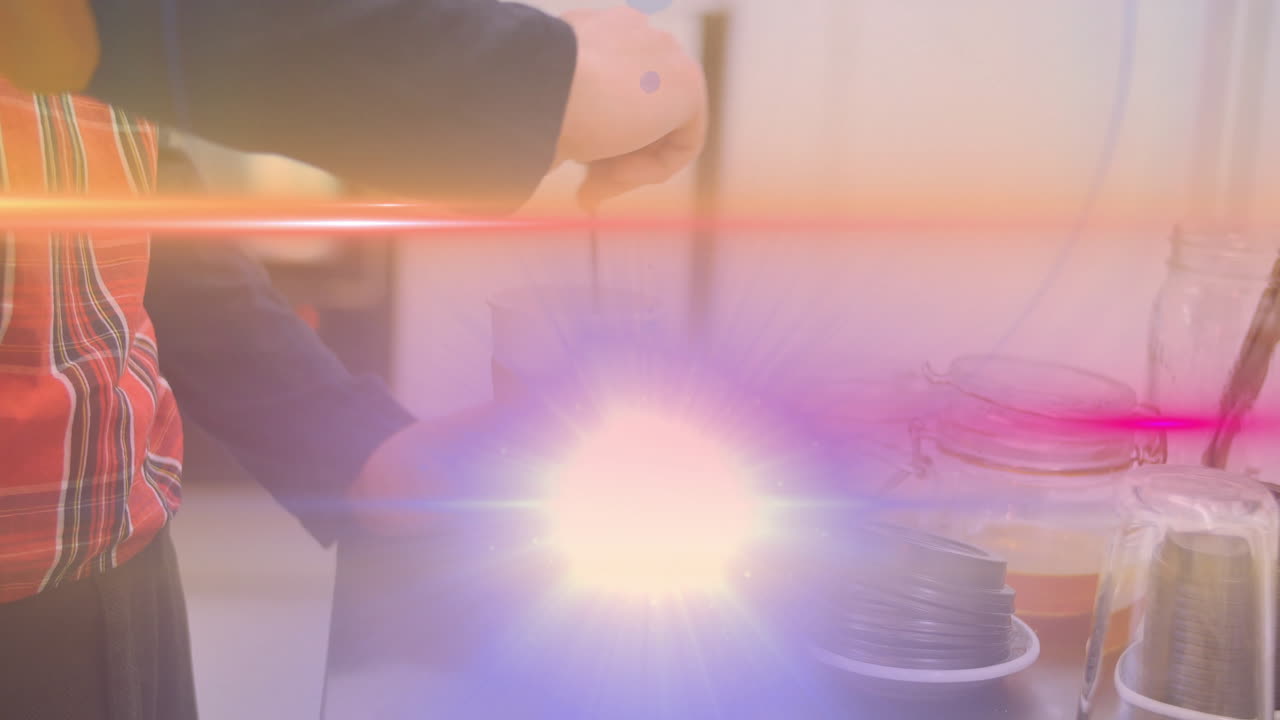 Person wearing plaid shirt reaching toward food containers on countertop under colorful lens flare