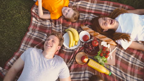 top view of happy family lying on blanket in park, laughing and having fun together while having a picnic in the park