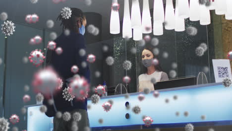 animation of covid 19 cells over diverse man and woman wearing face masks in hotel reception