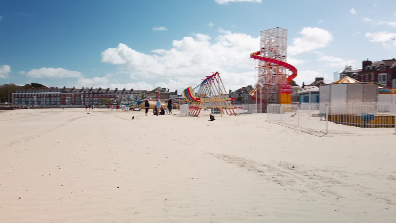 A crow takes flight at Weymouth Beach in England. It features a fairground on brilliant  yellow sand and perfect blue skies with just a few clouds