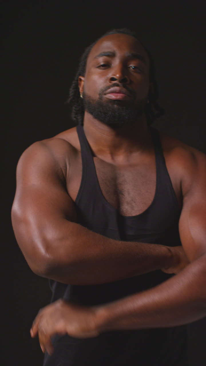 retrato de video vertical de un atleta masculino serio que lleva un chaleco de fitness con físico muscular caminando hacia la cámara y en el enfoque de entrenamiento para un evento deportivo contra un fondo de estudio negro
